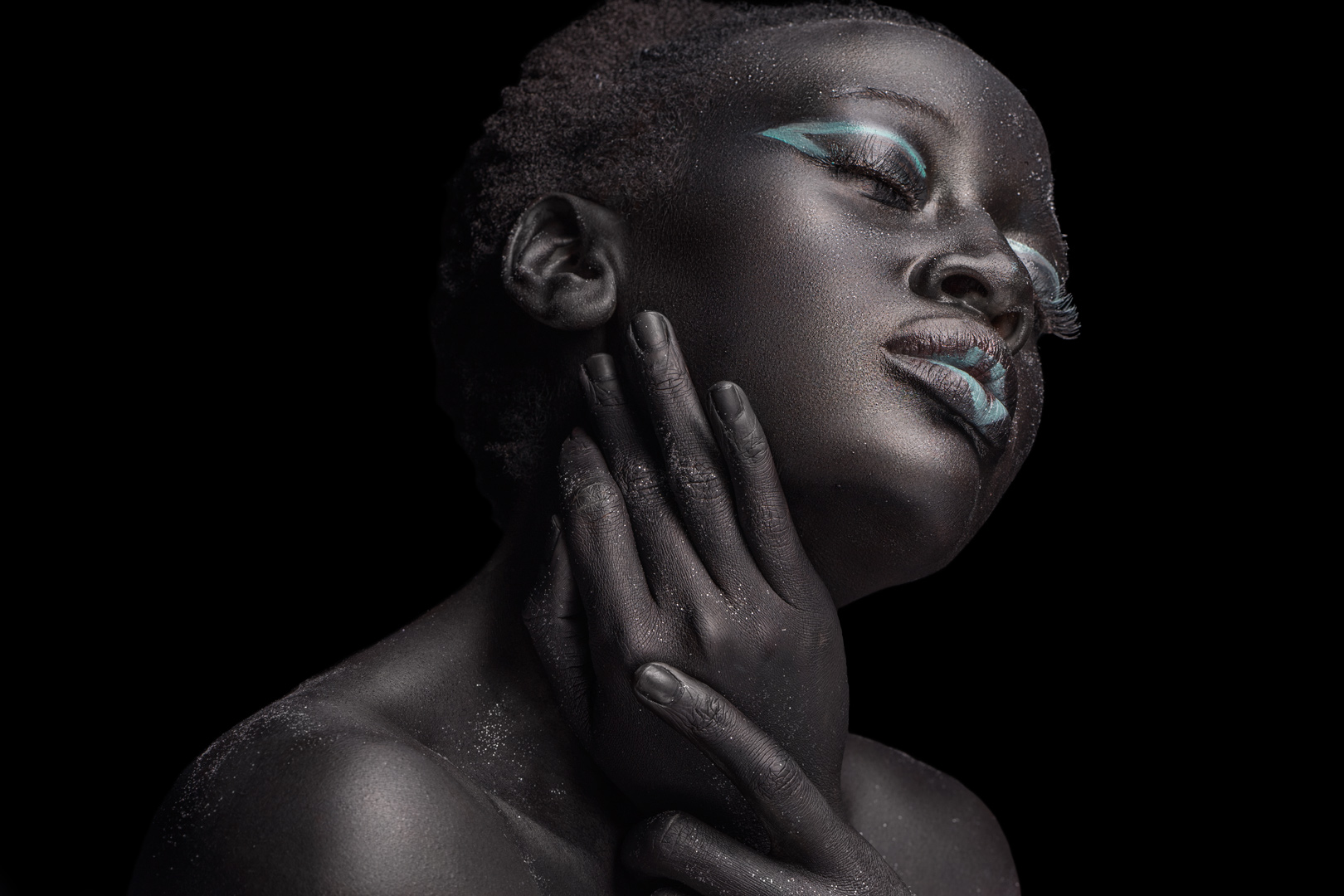 Profile beauty portrait with glitter-dusted skin and teal eyeliner against a black background