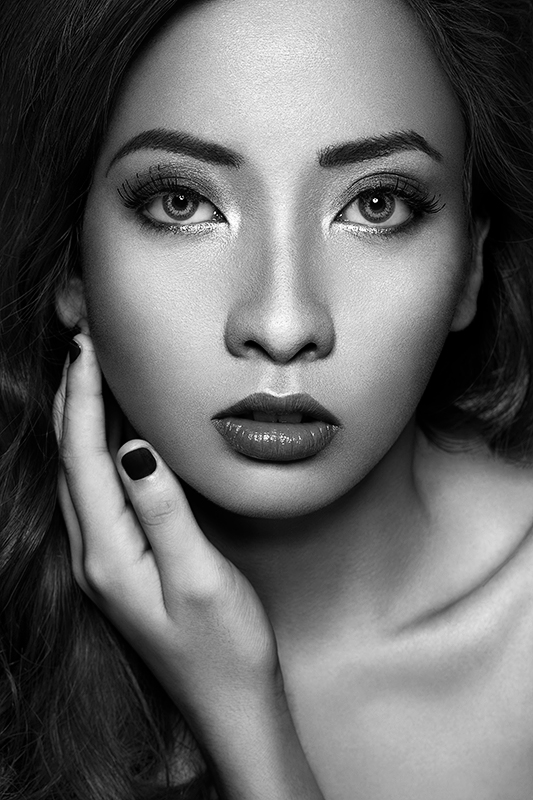 Black and white close-up beauty portrait with direct gaze, glitter eyeshadow, and dark nail polish