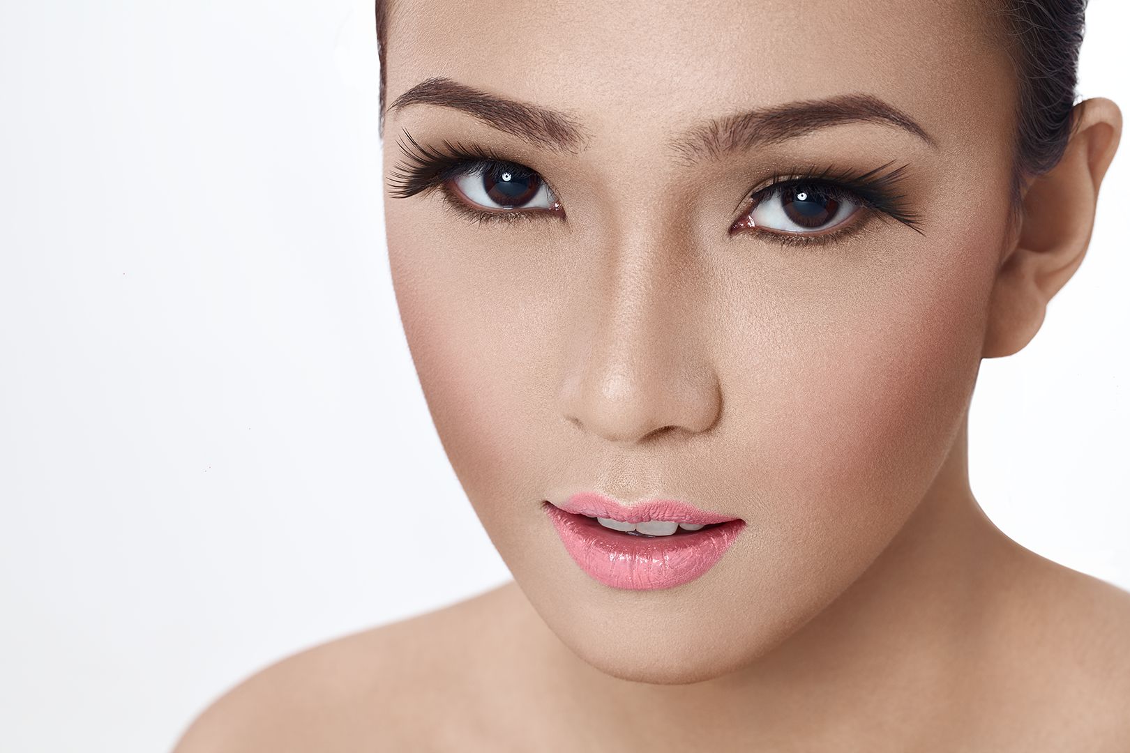 Extreme close-up beauty portrait showing natural skin texture, pink lips, and defined lashes against white