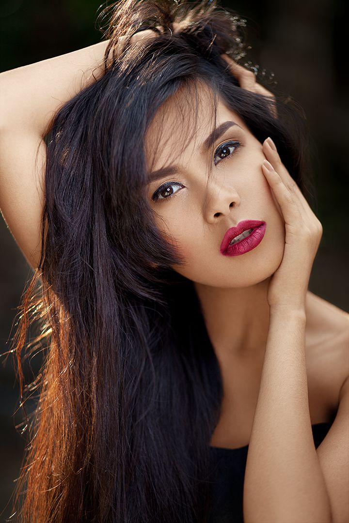Outdoor beauty portrait with berry-red lips and hands running through dark hair, natural backlight