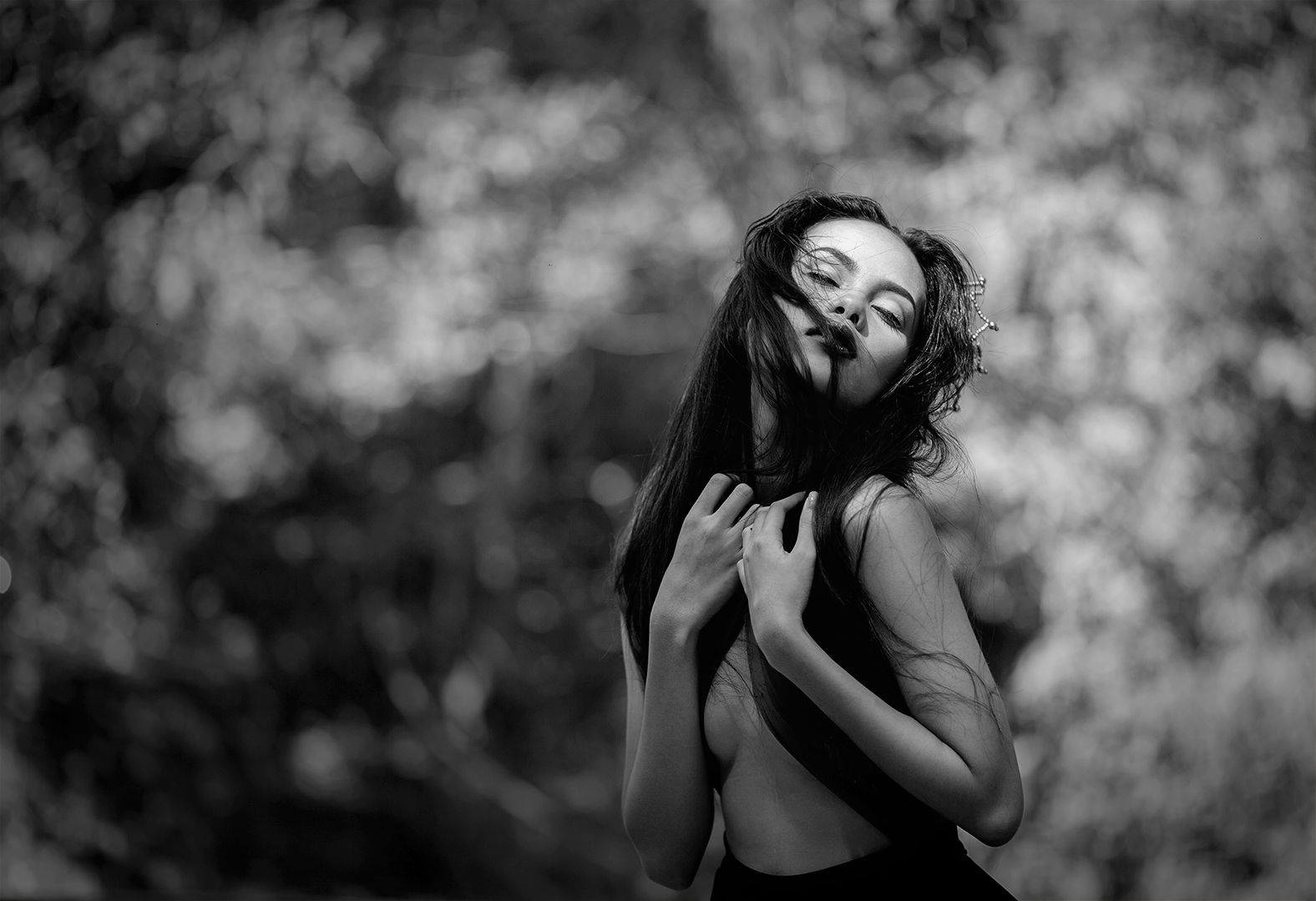 Black and white outdoor editorial with windswept hair, eyes closed, and delicate chain hair accessory