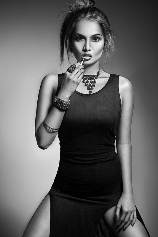 Black and white fashion portrait in black dress with statement necklace, applying lipstick